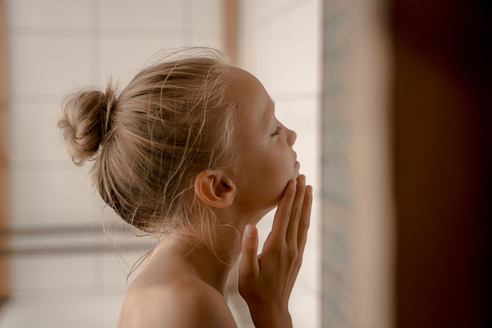 A young girl looking at her reflection in a mirror during a skincare routine, illustrating the rise of cosmeticorexia in children